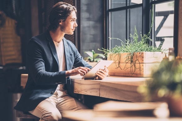 Confident young man in smart casual wear holding digital tablet while sitting near window in cafe - Why Are Taurus Men So Emotional