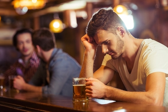 Sad young man in white t-shirt is looking at glass of beer while sitting at bar counter in pub - Why Are Taurus Men So Emotional